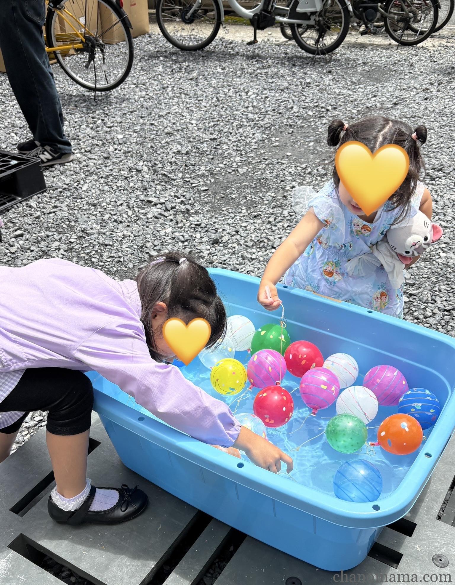 大塩するめ倉庫大解放市のヨーヨー釣りコーナー。青いたらいにカラフルなボールが並ぶ中、娘たちが挑戦している様子